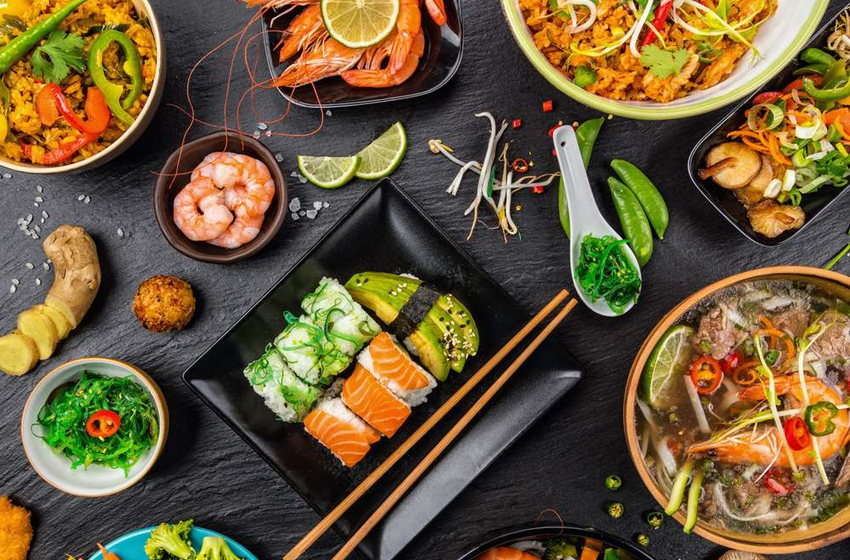 camarão, sushi e demias pratos de comidas típicas asiáticas dispostos em uma mesa de fundo preto