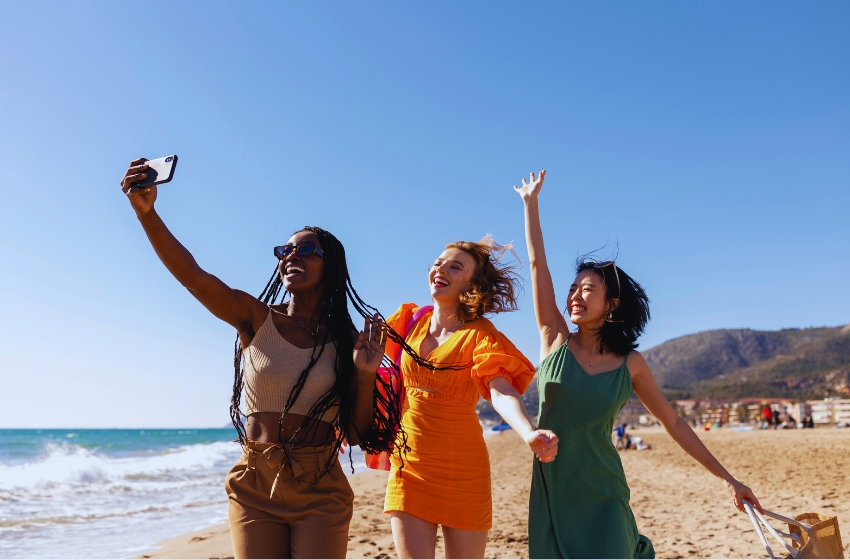 três amigas felizes posando para foto na praia