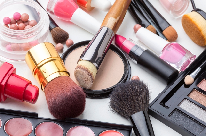 batom, blush, sombras, pó compacto, esmaltes e pincéis de maquiagem dispostos em um fundo branco