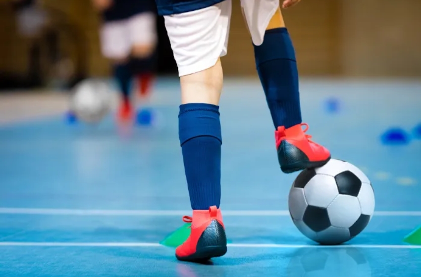menino usando chuteira e brincando com bola em quadra de futsal