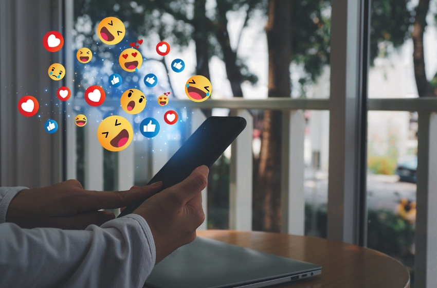 pessoa mexendo em um celular com vários emojis saindo da tela