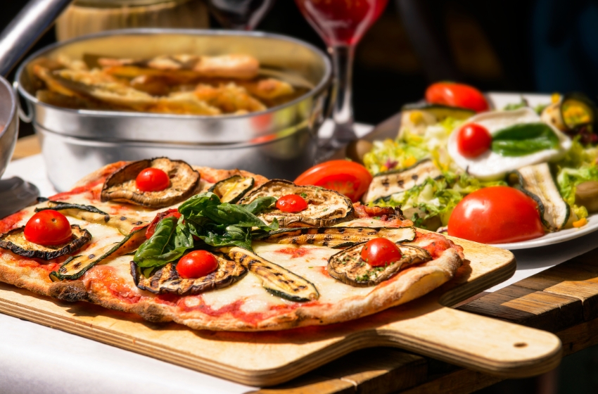 pizza com manjericão, queijo e tomates em cima de uma tábua