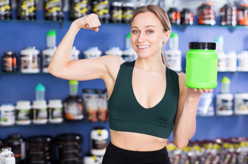 mulher exibindo o shape segurando um recipiente de suplementos de academia