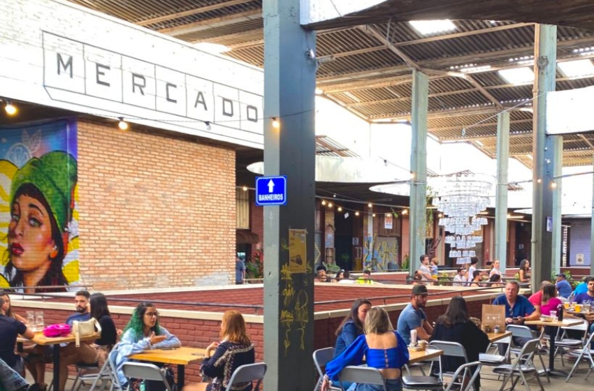 Pessoas sentadas nas mesas de uma praça de um mercado