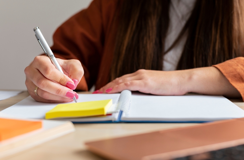 mulher segurando uma caneta e escrevendo em um caderno