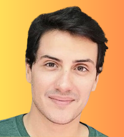 Na foto, vemos um homem branco, de cabelos pretos e blusa verde. Ele está sorridente, com uma grande quantidade de violetas em fundo. Este é Pedro Gazzinelli, coproprietário da Confeitaria Avellan.